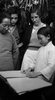 Child reading, while pastor and missionary students look on, [ca 1920s]. Credit: Walmsley Family.